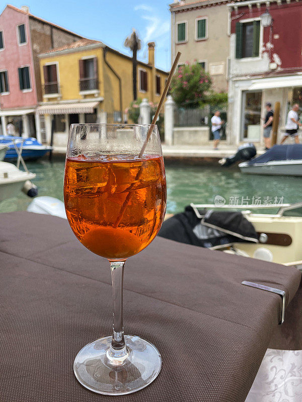 Spritz Veneziano鸡尾酒在玻璃中装饰着橄榄木棒，普罗赛克，消化苦味，苏打水和冰块，露天用餐环境，威尼斯运河背景，重点在前景